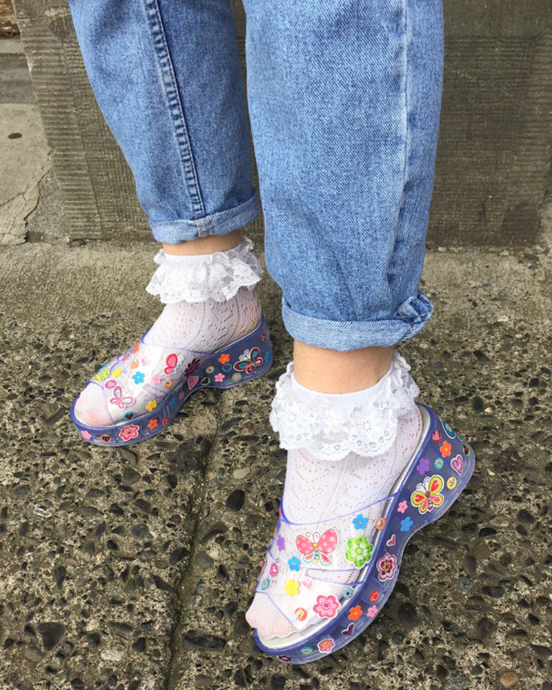 Person wearing frilly socks and jelly sandals decorated with novelty stickers
