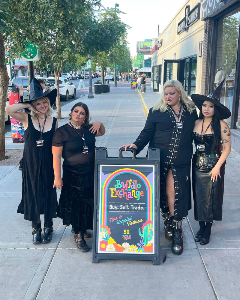 Group of people in all black witch outfits posing next to Buffalo Exchange sandwich board